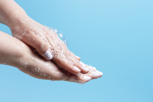 女孩用肥皂和白色泡沫洗手在蓝色背景上的特写。图片下载