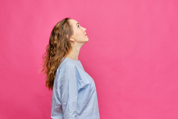 穿着淡蓝色t恤的时髦白人女孩微笑着抬头看着粉红色的背景。副本的空间。图片下载