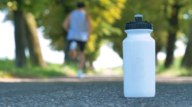一个运动白色的饮料瓶站在柏油路上，背景穿过街道上的一个男人图片下载
