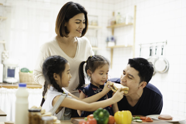 年轻的亚裔爱家正在厨房里准备做饭的早餐，桌上放着三明治蔬菜，兴奋的微笑着，感觉很幸福。女儿给父亲喂饭图片下载