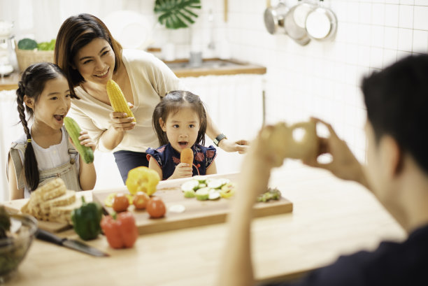 年轻的亚洲爱的家庭正在厨房里准备早餐。爸爸用面包自拍了一张照片。兴奋的微笑和快乐的感觉。父母教女儿在家里做饭。图片下载