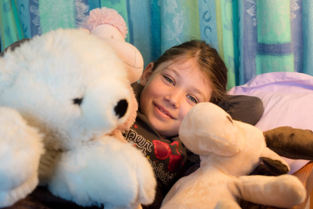 可爱的小女孩在床上抱着她的毛绒玩具图片下载