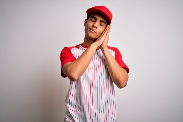 年轻英俊的非裔美国运动员穿着条纹棒球t恤和帽子睡累了做梦和摆姿势与手一起而闭上眼睛微笑。图片下载