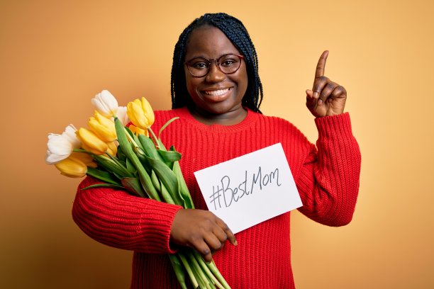 身材丰满的非裔美国妇女在母亲节拿着最好的妈妈信息和郁金香惊讶地提出一个想法或问题用快乐的脸指着手指，第一图片下载