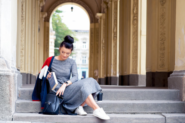 学生成年女孩把一本书放进大学楼梯上的黑色背包里。图片下载