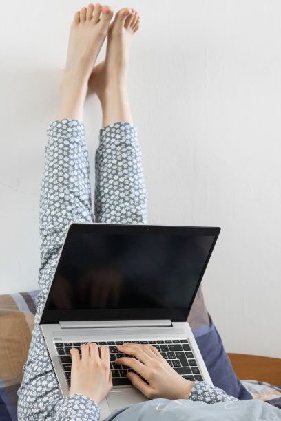女人翘着腿躺着，在笔记本电脑前工作。冠状病毒大流行期间的家庭办公概念。在笔记本上打字。图片下载