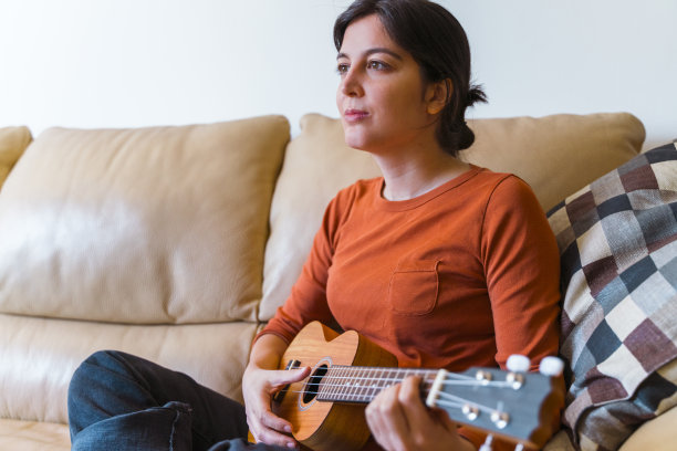 一个女人在沙发上玩尤克里里的侧视图。图片下载