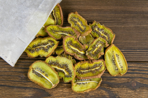 一张晒干的猕猴桃的照片从牛皮纸纸袋里掉出来，落在深色的木板上图片下载