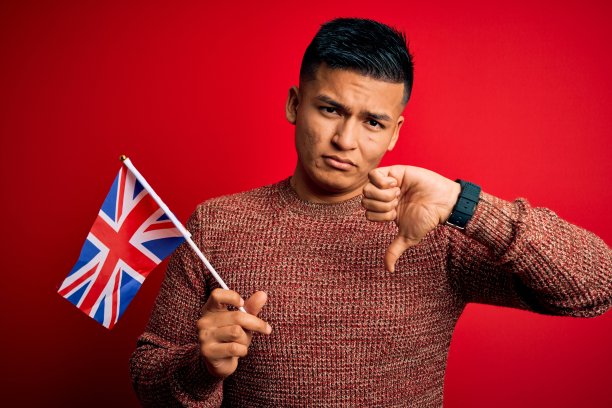 年轻英俊的拉丁男子穿着英国国旗在红色背景与愤怒的脸，消极的迹象显示不喜欢与拇指向下，拒绝概念图片下载