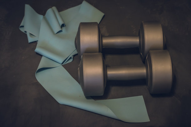 哑铃和橡皮筋的健身在一个深灰色的石头背景，地方为您的文本。家庭运动拷贝空间图片下载