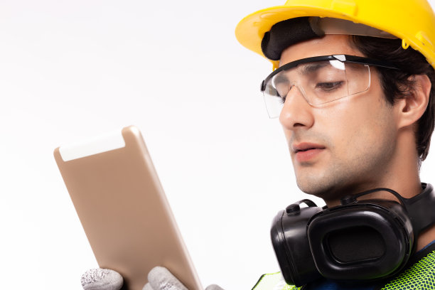 在工作场所或工业中使用数字平板电脑的工程师。年轻英俊的产业工人都戴安全帽、安全手套、安全眼镜、耳机。蓝领工人。孤立在白色图片下载