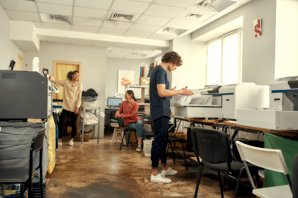 快速优质的服务。年轻快乐的千禧一代在工作场所使用热压转印机打印t恤的全长照片图片下载