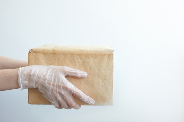 带医用手套的快递员给顾客一个包裹。隔离中的交付服务。新冠肺炎大流行的影响。快递员拿着一个纸板箱在白色背景下图片下载