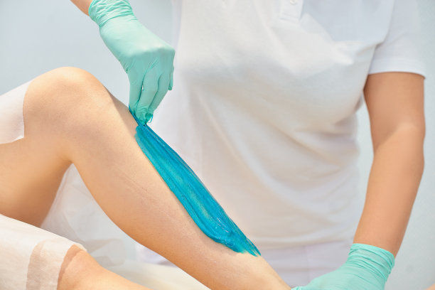 脱毛美容概念-美容师在水疗中心用液体糖为年轻女性脱毛。用绿松石舒肤膏去除腿部毛发图片下载