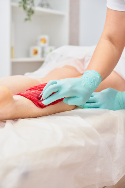 脱毛和美容概念-美容师蜡年轻女子与液体糖水疗。用彩色舒汗膏脱毛图片下载