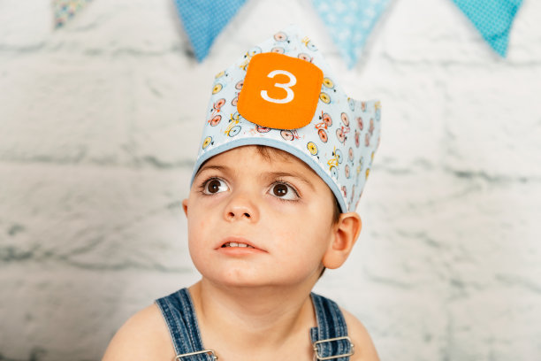 拍摄生日照片的男孩，已经3岁了，身体和智力都有缺陷。他戴着皇冠坐在地上。工作室背景墙，木材图片下载