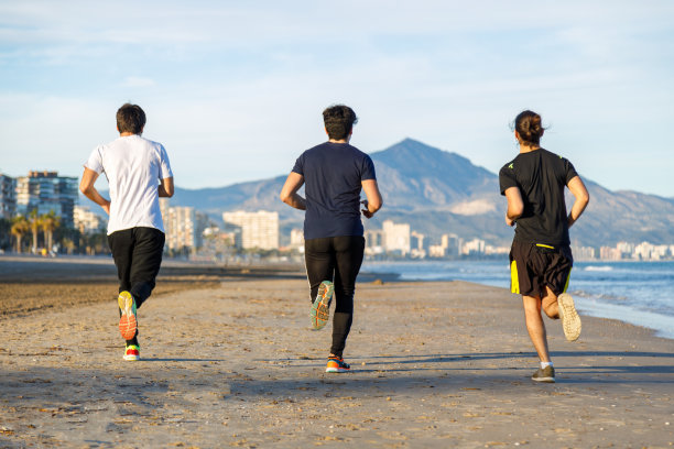 三个年轻男人在日落时沿着海滩奔跑（背影）素材图片