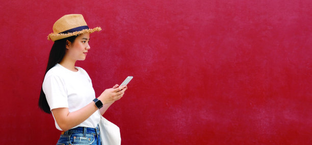 快乐的亚洲女孩使用手机站在红墙背景与拷贝空间，年轻的亚洲女人与智能手表手持智能手机在休闲的生活方式，美丽的时尚女性青少年和手机的肖像，人和技术的旗帜图片下载