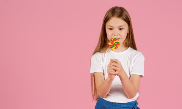 一个惊讶的小女孩的肖像拿着心形棒棒糖，看着孤立的相机在粉红色的背景图片下载