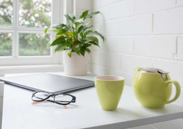 茶壶和茶杯放在家庭办公桌上，配有眼镜和闭合的笔记本电脑图片下载