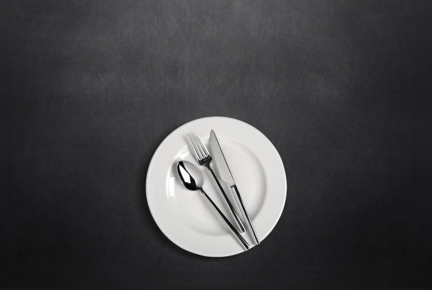 白色的盘子，叉子，勺子和刀叉放在深色的桌子上图片下载