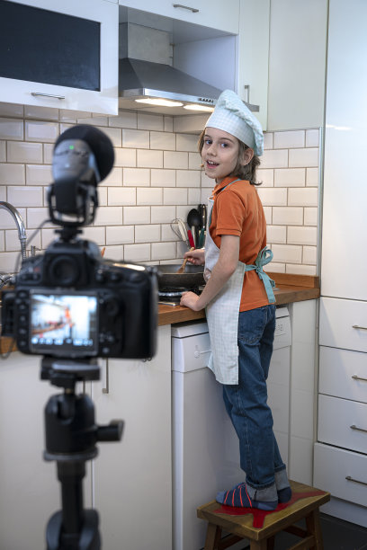 在厨房里，孩子在三脚架上的摄像机上录音。图片下载