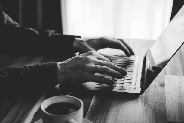 一个男人正在笔记本电脑的键盘上打字。在家工作的概念，黑白照片。图片下载