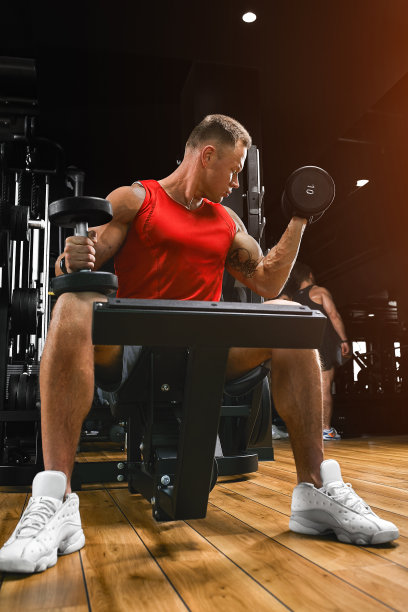 一个赤裸上身的肌肉男正在做二头肌练习，哑铃练习是他健美锻炼的一部分。健身动机，运动生活方式，健康，运动身体，身体积极。薄膜颗粒，选择性聚焦图片下载