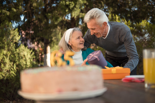 快乐的老年妇女收到礼物，从她的丈夫在一个生日聚会上在家后院。丈夫亲吻妻子图片下载