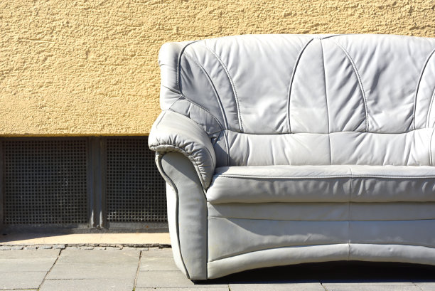 在德国，一个明亮的旧皮沙发伫立在一堵带有地下室窗户的房子墙前，在路边，它邀请你坐下图片下载