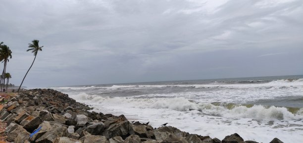 一幅有岩石和椰子树的海滩图片，背景是多云的天空。这幅画里的大海波涛汹涌。喀拉拉邦卡皮尔海滩(瓦尔卡拉镇)。图片下载