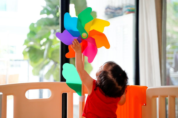 快乐的婴儿与色彩缤纷的风车，幼童试图处理在游戏室的隔墙风车针，家。图片下载