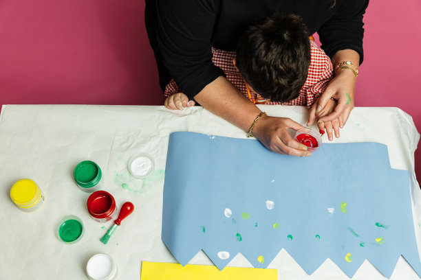 在校特殊教育老师和学生用丙烯颜料在桌子上共同绘制生日花环和黄色纸板，进行塑料工艺疗法图片下载