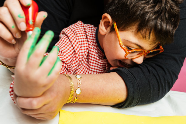 在校特殊教育老师和学生用丙烯颜料在桌子上共同绘制生日花环和黄色纸板，进行塑料工艺疗法图片下载