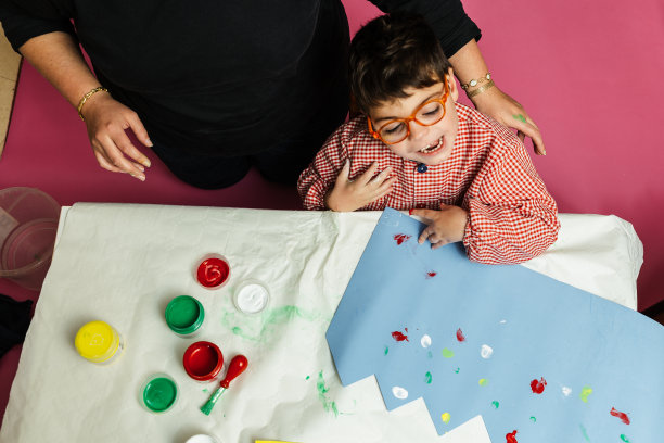 在校特殊教育老师和学生用丙烯颜料在桌子上共同绘制生日花环和黄色纸板，进行塑料工艺疗法图片下载