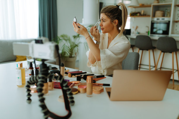 照片美丽的女人用马尾辫化妆，而看着方便的镜子。年轻女子记录她的美容博客关于化妆和化妆品在家。图片下载