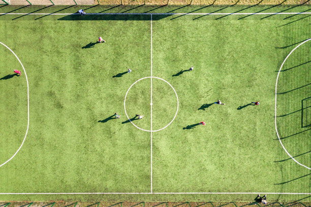 从上到下鸟瞰绿色足球场和球员踢足球。无人机拍摄的图像，小运动员在草地覆盖的体育场体育活动期间。图片下载