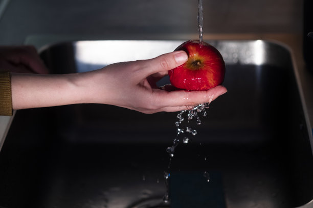 色彩和生动的照片，一个年轻的女人彻底清洗红苹果在厨房。准备吃的水果需要洗一下图片下载