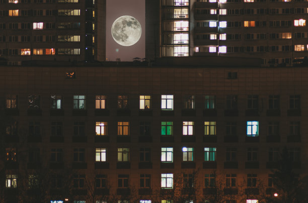 一个夜晚城市的景观，高楼大厦和灯光在居民的窗户和满月之间的房子图片下载