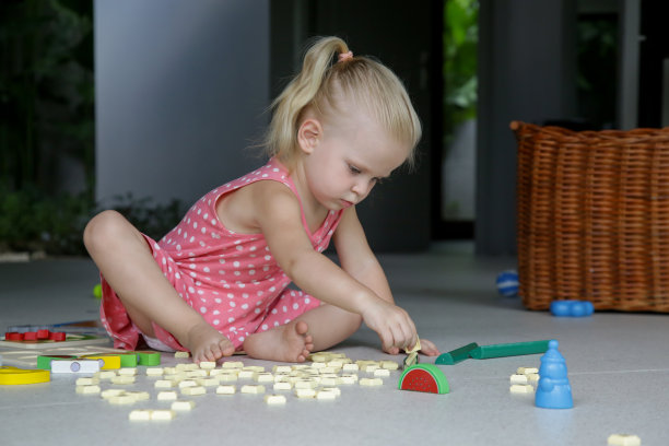 可爱的蹒跚学步的小女孩在地板上独自玩耍。两岁小孩玩玩具的偷拍照片。图片下载