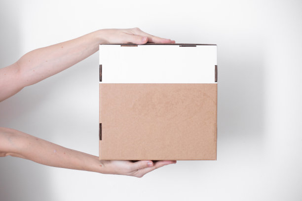 一个包裹纸箱在一个送货员的手在一个白色的背景。送货服务的概念。图片下载
