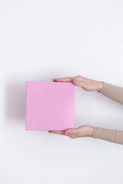 一个快递女手里拿着一个白色背景的粉色纸盒包裹。送货服务的概念。图片下载