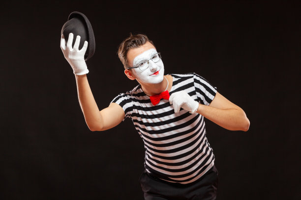 男性哑剧表演艺术家的肖像，孤立在黑色背景上。男人举起帽子，摸了摸领结。象征问候、介绍、友谊图片下载