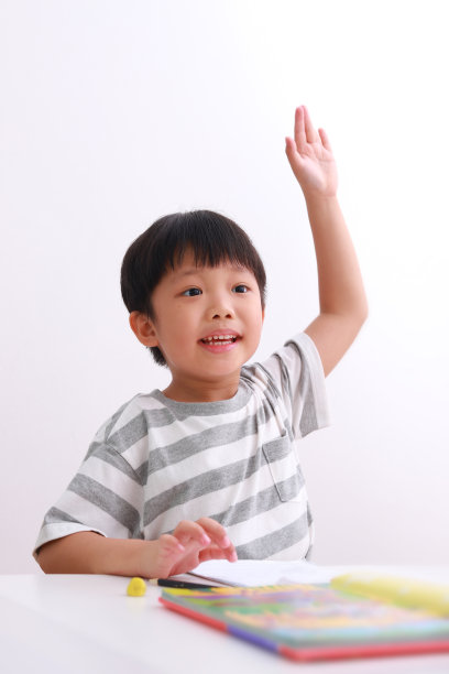 小男孩坐在书桌前做作业，背景是白色的。图片下载