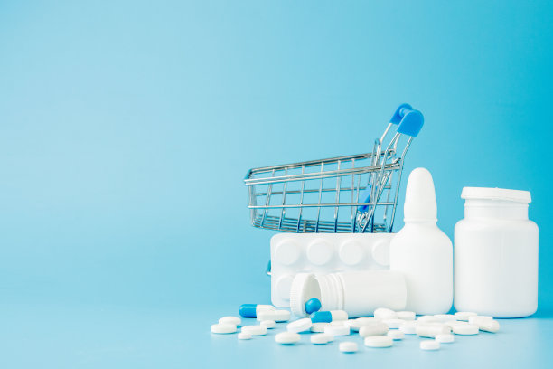 蓝色背景上散落着各种药片、药品、喷雾、瓶子、温度计、注射器和空的购物车。药房购物的概念图片下载
