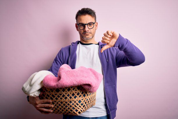 年轻英俊的男人在做家务时拿着柳条篮子，脸上带着愤怒，消极的迹象显示不喜欢用拇指向下，拒绝概念图片下载