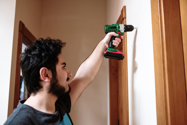 一个年轻人用钻头在墙上钻了一个洞图片下载