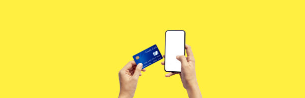 手持蓝色信用卡使用智能手机的女人孤立在黄色背景下，正面视图。蓝色的银行卡设计模型。移动支付，网上购物概念图片下载