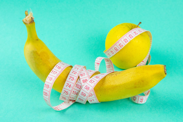 不同种类的水果，比如苹果和香蕉，放在单脚的基础上，并用卷尺包裹起来——这是一种有趣的健康减肥理念图片下载