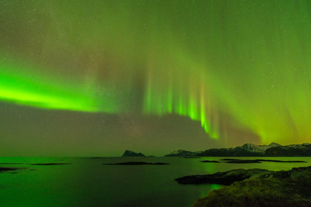 这是一张山水照片，有美丽的绿色北极光，在黑暗的星星点缀的天空中反射在海洋中图片下载